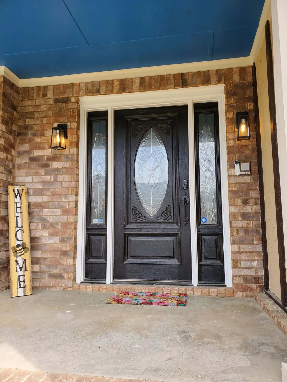 The image showcases the inviting exterior of a lakeside single-family home, featuring a decorative front door adorned with a cheerful welcome sign and a vibrant, colorful doormat. The entryway hints at warm hospitality and memorable gatherings, setting the tone for a relaxing lakeside escape.