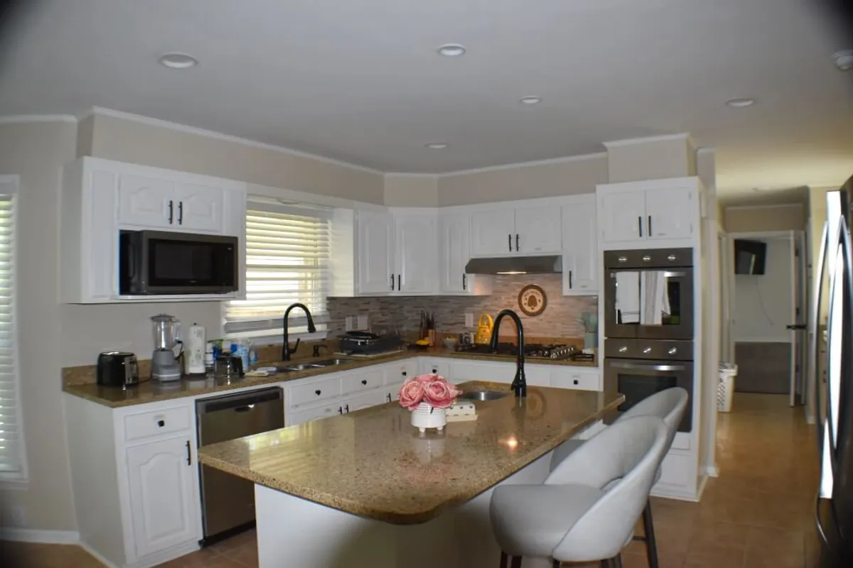 A warm kitchen scene with a granite countertop, stainless steel appliances, and a floral centerpiece, suggesting both functionality and hospitality. The ambiance feels perfect for baking, entertaining, or casual family breakfasts.
