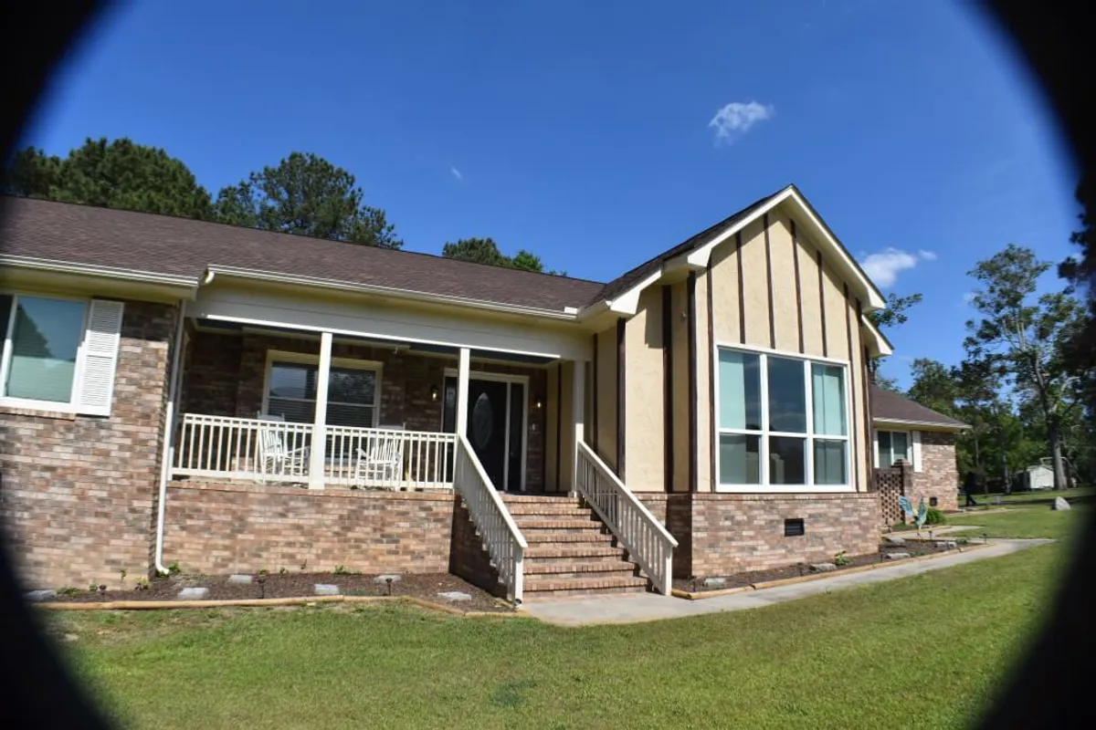 This exterior shot captures the front porch area with large windows and a staircase leading up to it. The porch is spacious and inviting, ideal for gatherings, enjoying coffee at sunrise, or unwinding in the evening as the sun sets.
