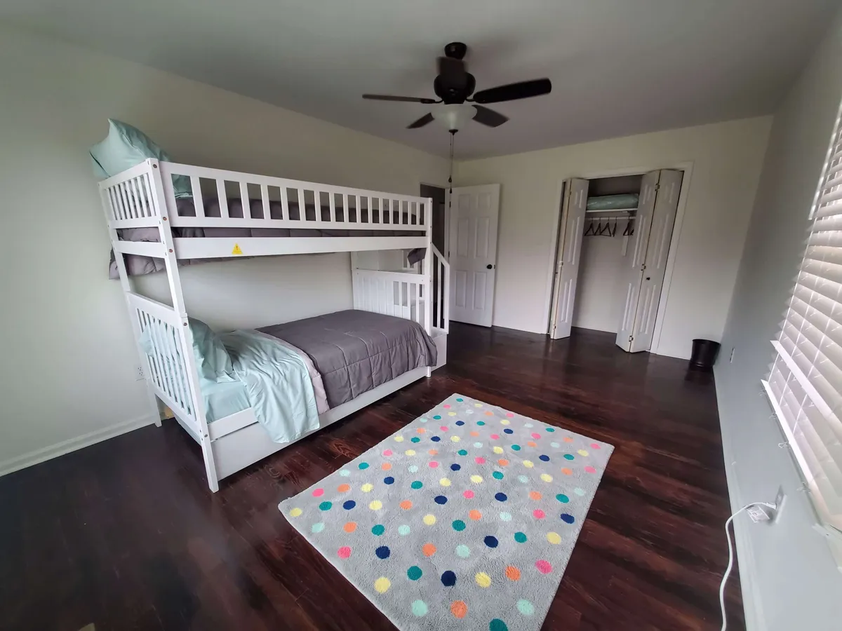A cheerful bunk room with a sturdy bunk bed, colorful rug, and ceiling fan. The lower bunk is styled for comfort and the overall atmosphere is playful yet cozy, perfect for children's adventures and late-night whispers.