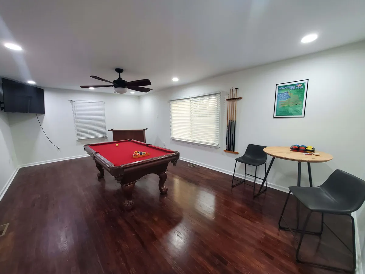 A game room featuring a pool table, small table and chairs, a wall-mounted TV, and a cue rack. The space feels casual and welcoming—designed for friendly competition and shared laughter.