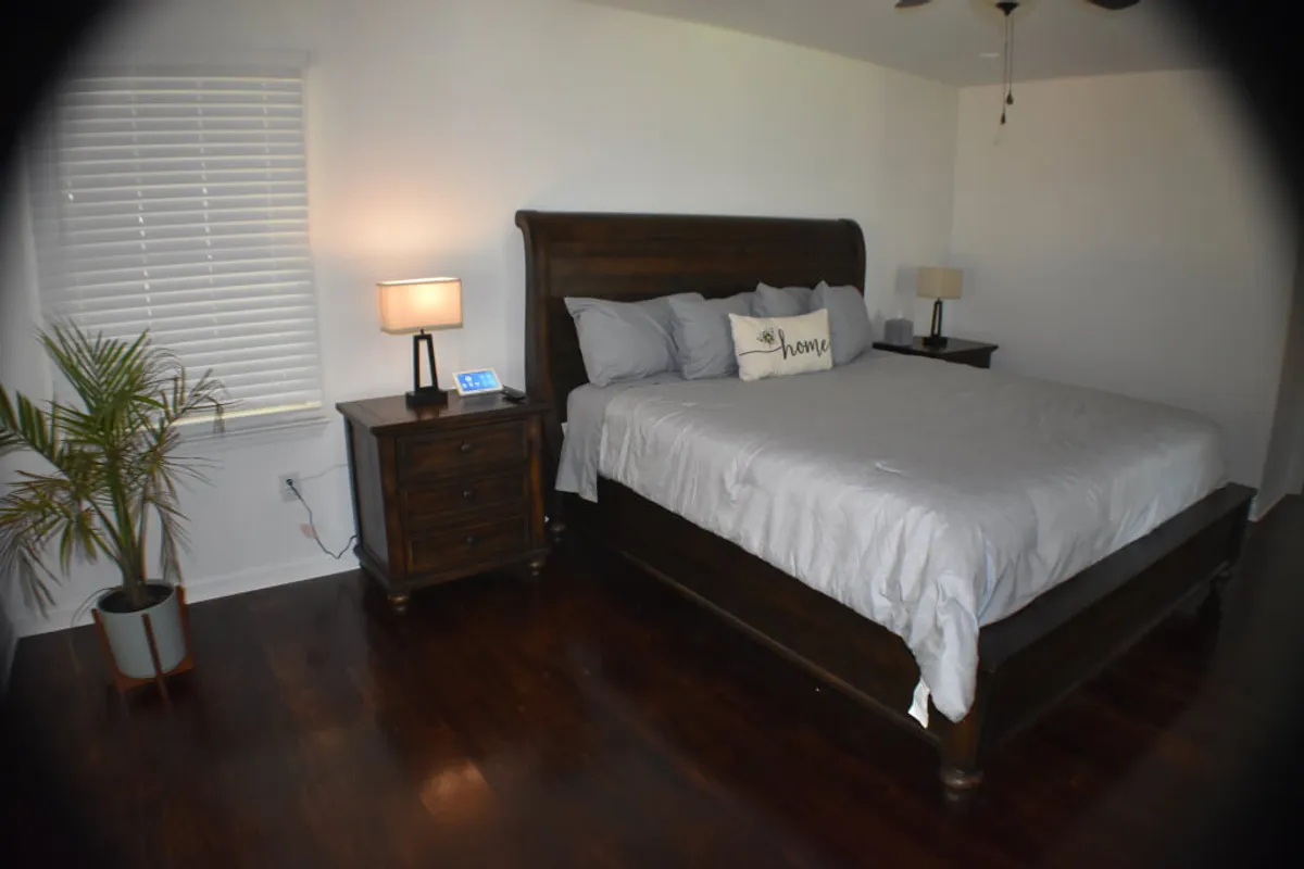 A cozy bedroom with a plush bed, nightstand, potted plant, and soft lighting from a bedside lamp. The mood is warm and inviting—ideal for unwinding with a book or enjoying a peaceful night’s rest.