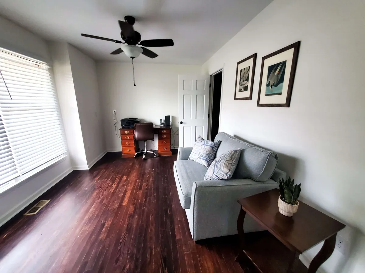 A cozy office or study area is shown with a comfortable sofa, a work desk, attractive artwork, and a leafy plant. The room is filled with natural light, suggesting a quiet corner for reflection or remote work.