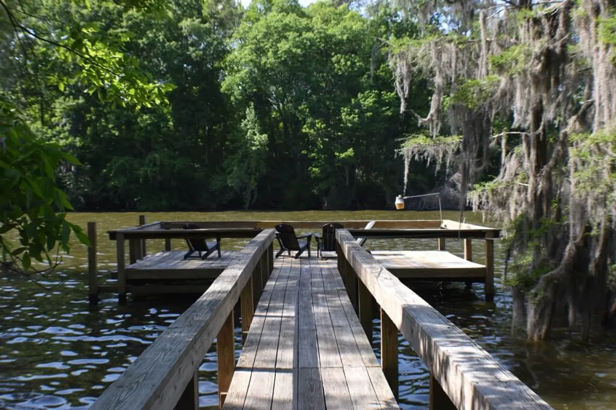 This exterior image displays a private wooden dock extending over calm water, surrounded by lush greenery. The scene is serene and beckons for fishing, boating, or quiet stargazing, perfectly capturing lakeside living.